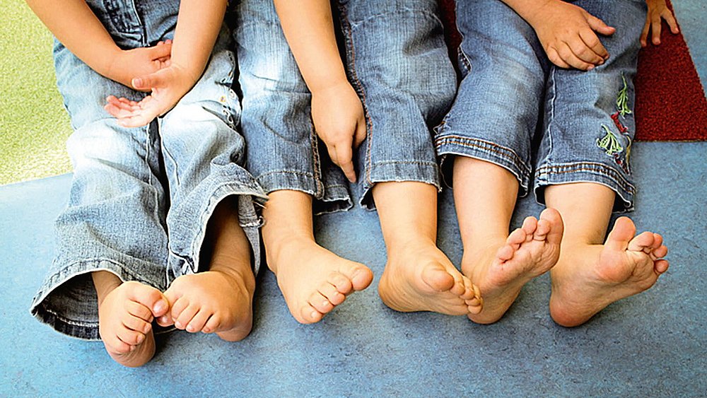 Füße von drei Kindern in Jeans sitzend auf einem Boden. 