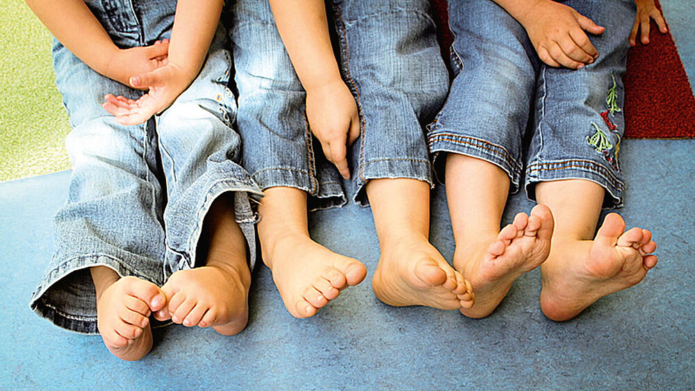 Füße von drei Kindern in Jeans sitzend auf einem Boden.