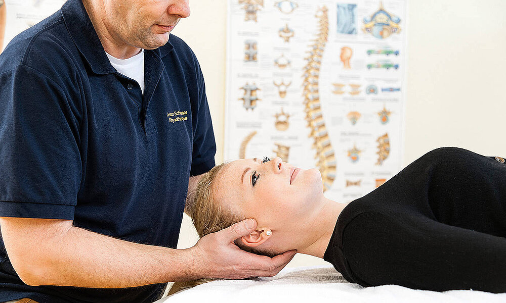 Physiotherapeut behandelt eine Frau am Hinterkopf, die auf dem Rücken liegt.