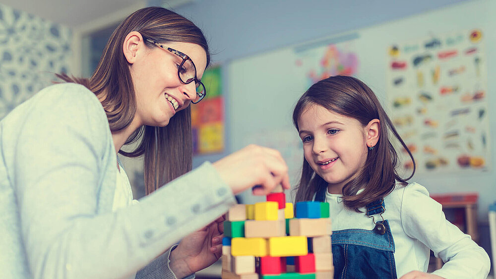 Pädagogische Fachkraft spielt mit einem Mädchen mit Bauklötzen.
