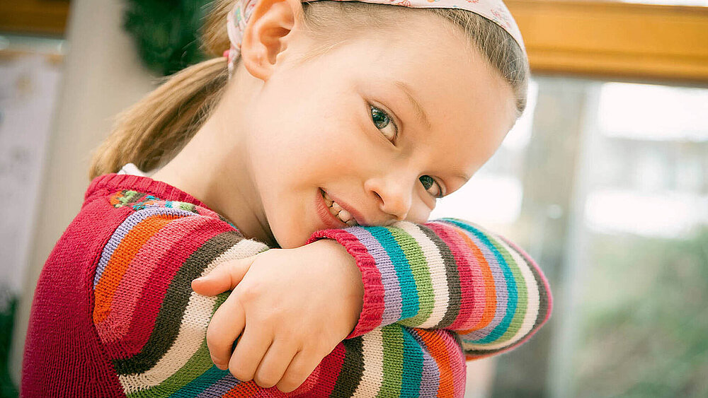 Mädchen mit buntem Pullover schaut direkt in die Kamera.