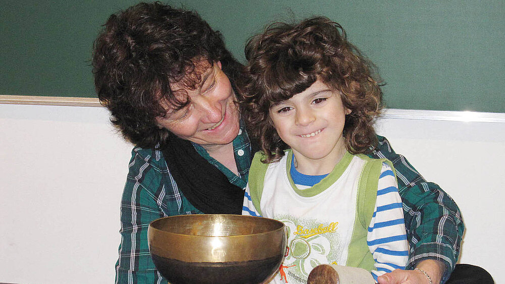 Eine pädagogische Kraft und ein Kind haben eine Klangschale in den Händen