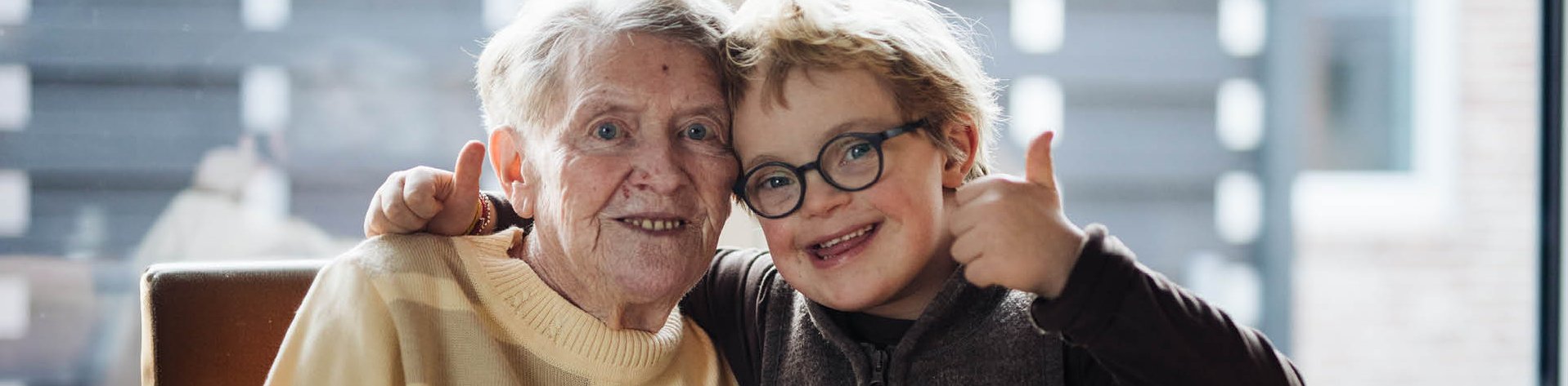 Eine ältere Frau Arm in Arm mit einem Jungen mit Trisomie 21.