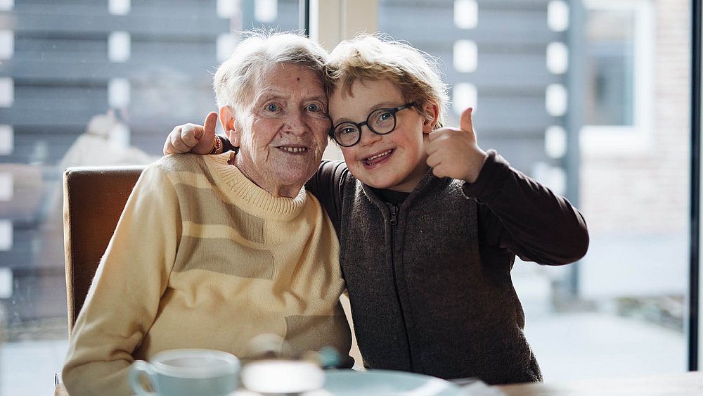 Eine ältere Frau Arm in Arm mit einem Jungen mit Trisomie 21.
